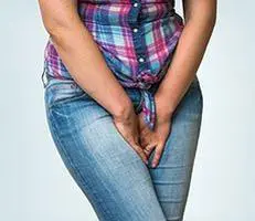 Person in jeans and plaid shirt holding abdomen.