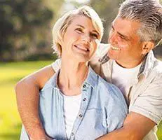 Older couple smiling and embracing outdoors.