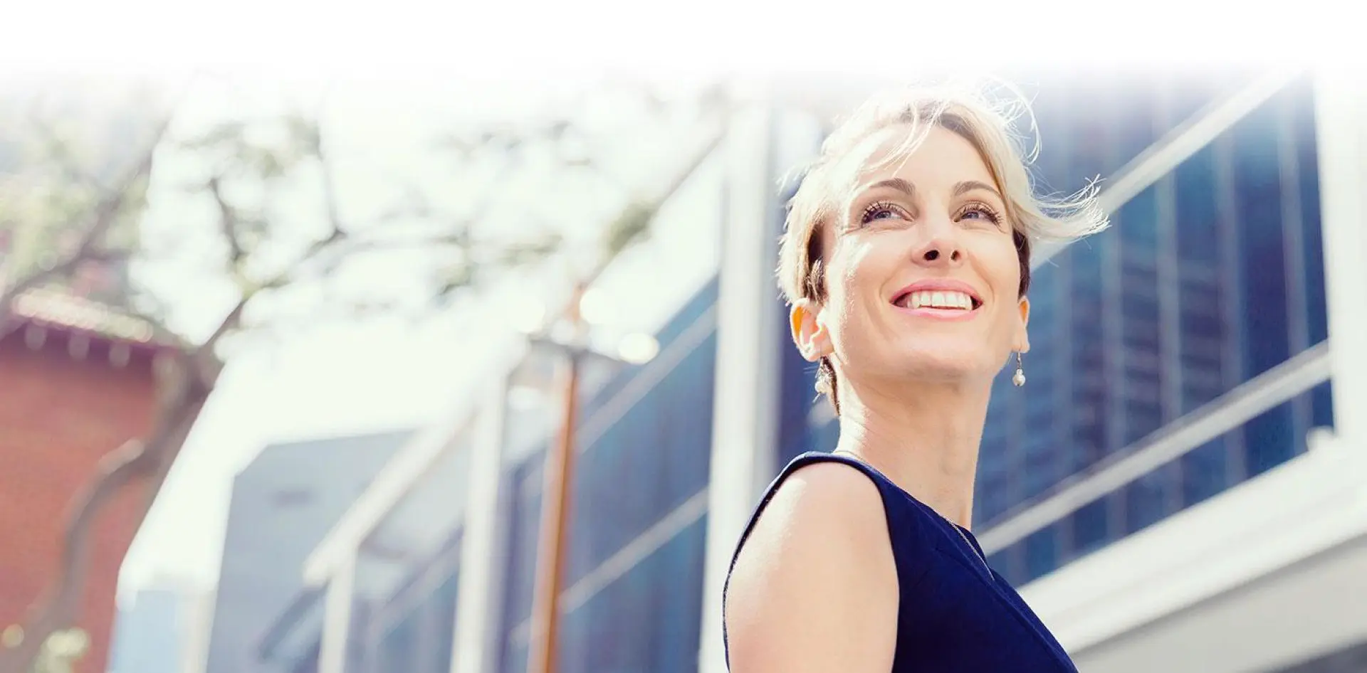 hero 01-1 Smiling woman outdoors near modern buildings.